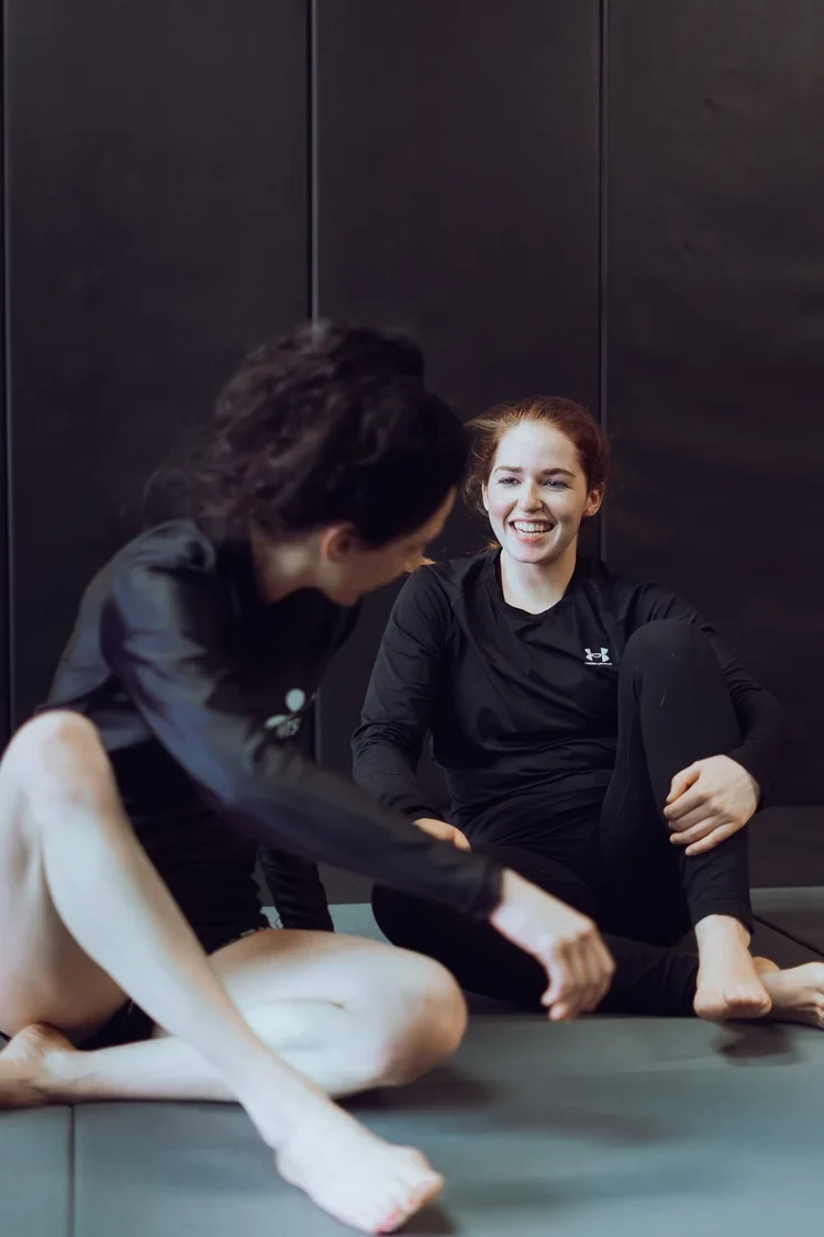 Two students relaxing and chatting on the mats after a class at Lucid Jiu Jitsu in Hewlett NY